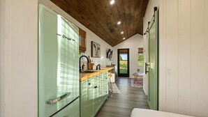 Una cocina estrecha con techo de madera, un refrigerador verde y encimera de madera.