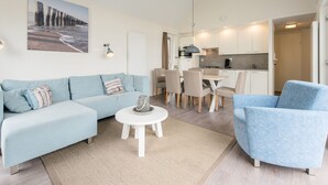 A modern living room with a light blue sofa, a matching armchair, and a dining area with a small table and chairs. - Modern Chalet Near the Coast (Hollum)