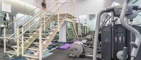 A gym with a staircase, exercise equipment, and a mirrored wall.