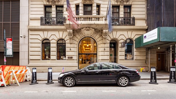 A black car parked in front of a historic building with ornate architecture, a prominent entrance, and flags.