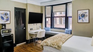 A hotel room with a bed, a desk, a chair, a TV, and a window with blinds.