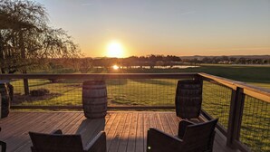 Un patio in legno con sedie in vimini e vista su un campo da golf al tramonto.
