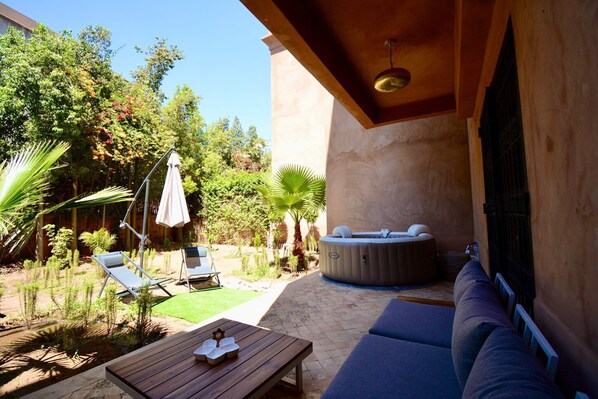 A patio area with a hot tub, lounge chairs, and a table.