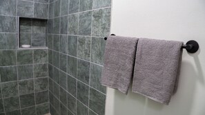 A bathroom with green tiles and two towels hanging on a black towel rack.