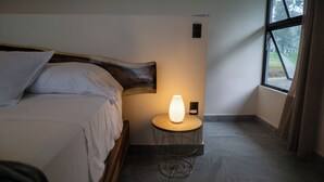 Una cama bien hecha con sábanas blancas, un cabecero de madera y una mesita de noche con una lámpara moderna.