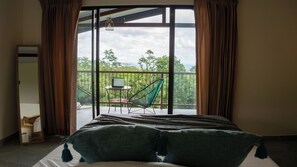 A bedroom with a large window, a bed, a chair, and a laptop on a small table. - Mountain cabin experience, enjoy unique sunrises (La Fortuna)