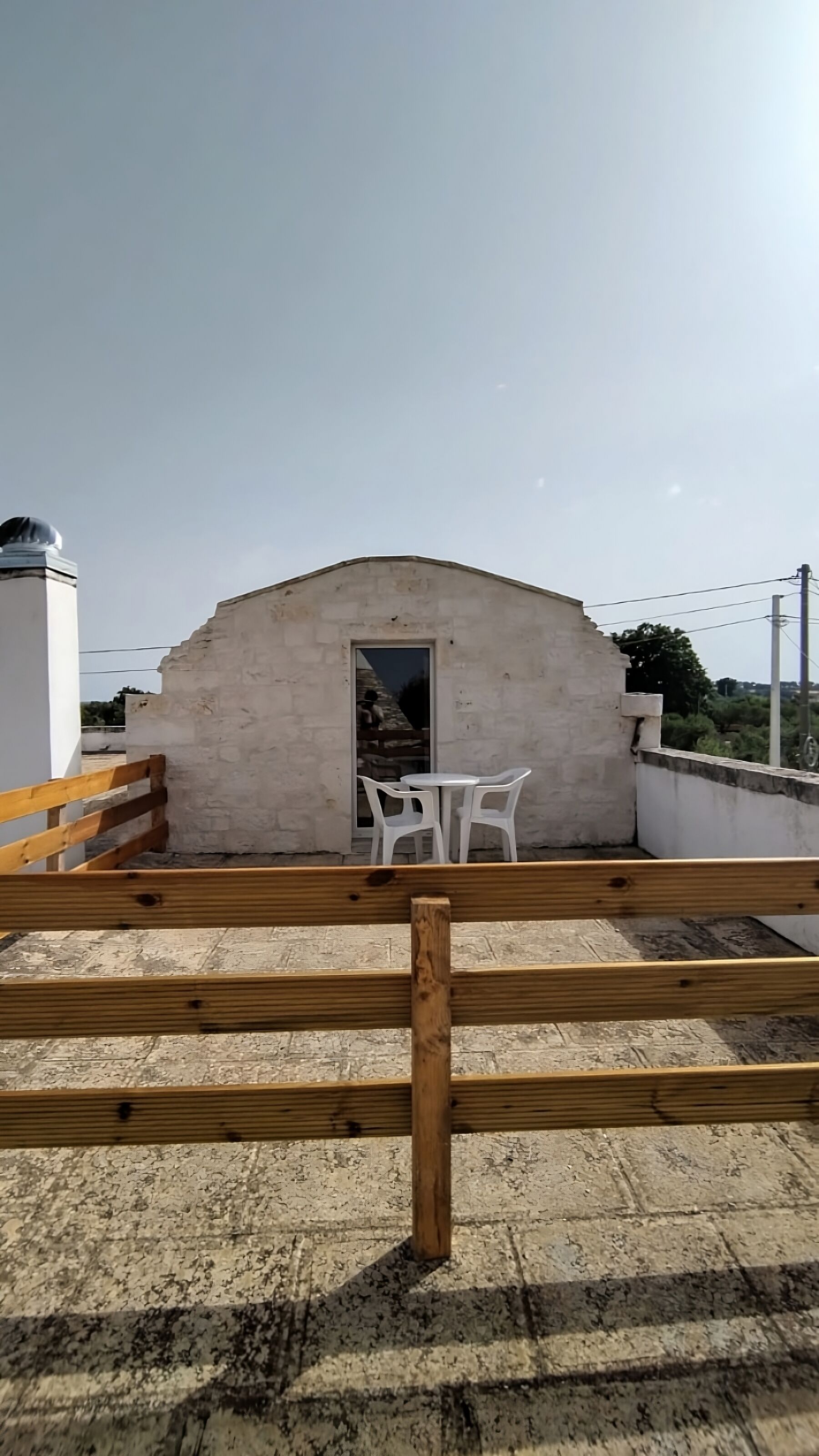 Eine Dachterrasse mit einer Steinmauer, einem Holzzaun und einem kleinen Tisch mit Stühlen.