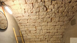 A bathroom with a stone wall, a white sink, a wooden shelf, a black faucet, a white toilet, and a ladder. - High Accommodation in LocoMura (Locorotondo)