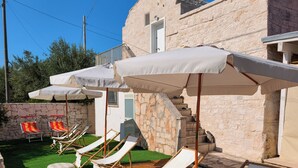 Une terrasse en bois avec des chaises longues et des parasols, un mur en pierre et un escalier menant à un bâtiment.