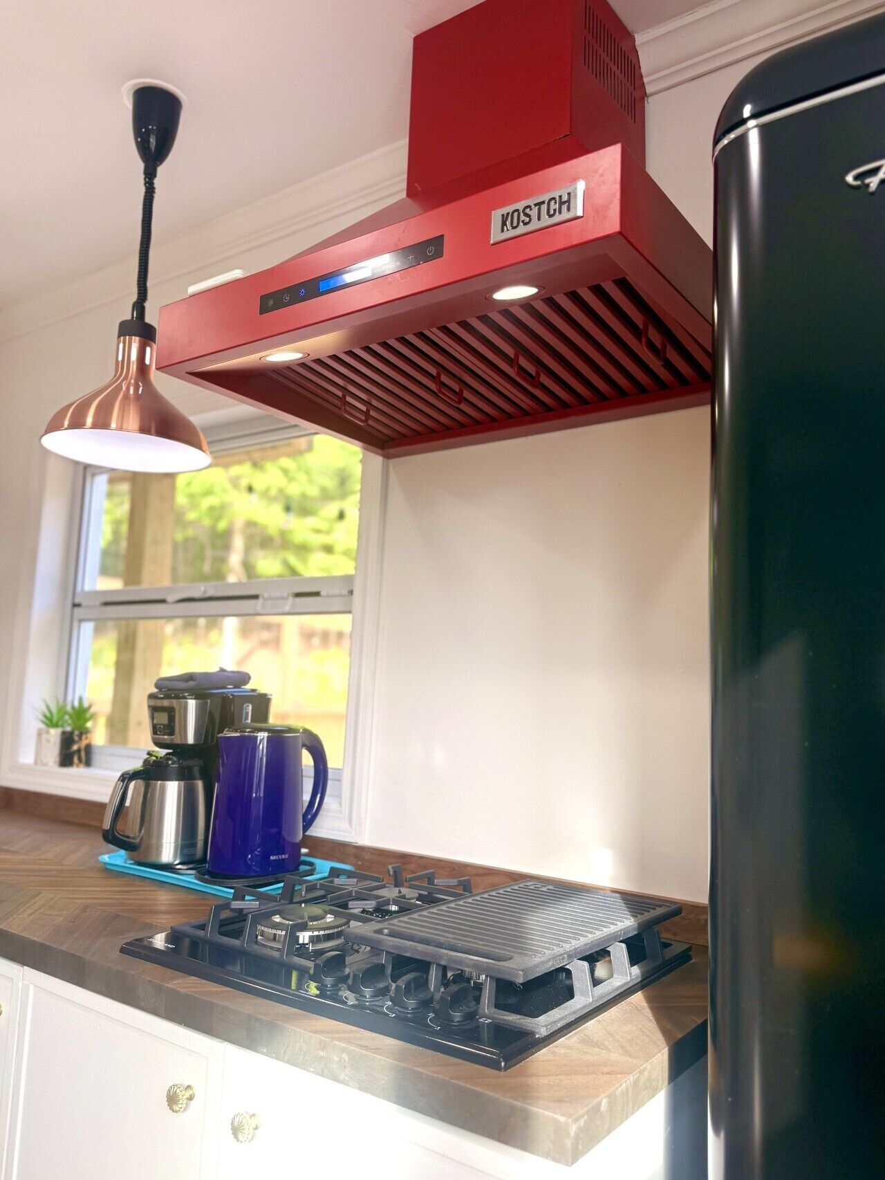 Une cuisine avec une hotte d’extraction rouge, une cuisinière en acier inoxydable et un réfrigérateur noir.