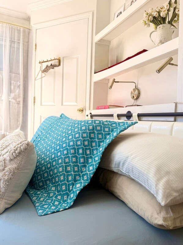 A bedroom with a bed, pillows, a nightstand, a shelf with books and a vase of flowers. - Catskills Apartment, Little Love Bird #5 (Highmount)