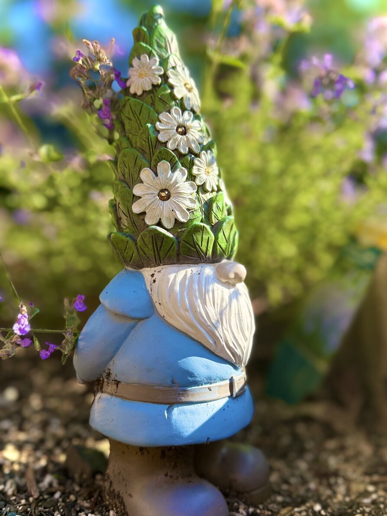 A decorative garden gnome with a blue skirt and white flowers on its head.