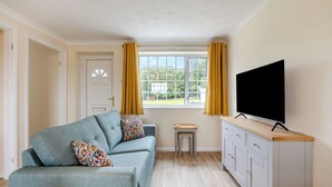 Een woonkamer met een bank, een televisie, een kast en een raam met gordijnen.