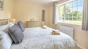 Een slaapkamer met een bed, nachtlampjes, een dressoir, een radiator en een raam met uitzicht op groen.