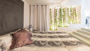 Un dormitorio moderno con cama, mesita de noche, lámpara y ventana con vistas al exterior.