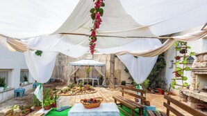 Un patio exterior con una mesa, bancos, plantas en macetas y un arreglo floral colgante.