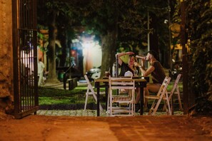 Een terras met een tafel en stoelen, omringd door groen en een hek.