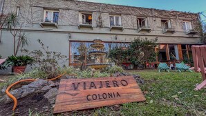 A wooden sign with "VIAJERO COLONIA" engraved, a multi-tiered fountain, and a building with balconies and windows.