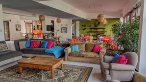 A spacious living room with a sofa set, a coffee table, and a dining area with colorful chairs and tables.