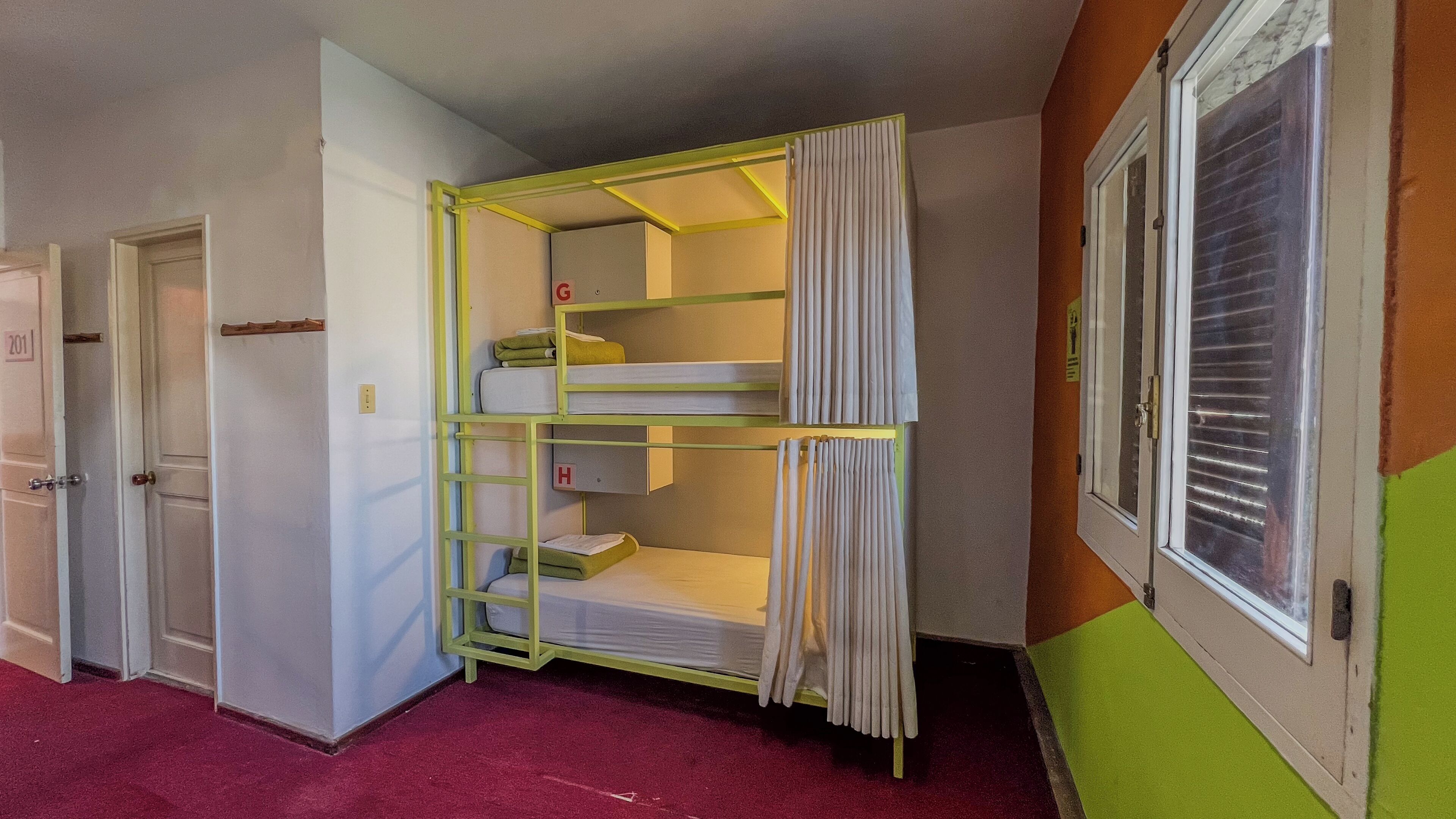 A room with a bunk bed, a door with a number, and a window with blinds.