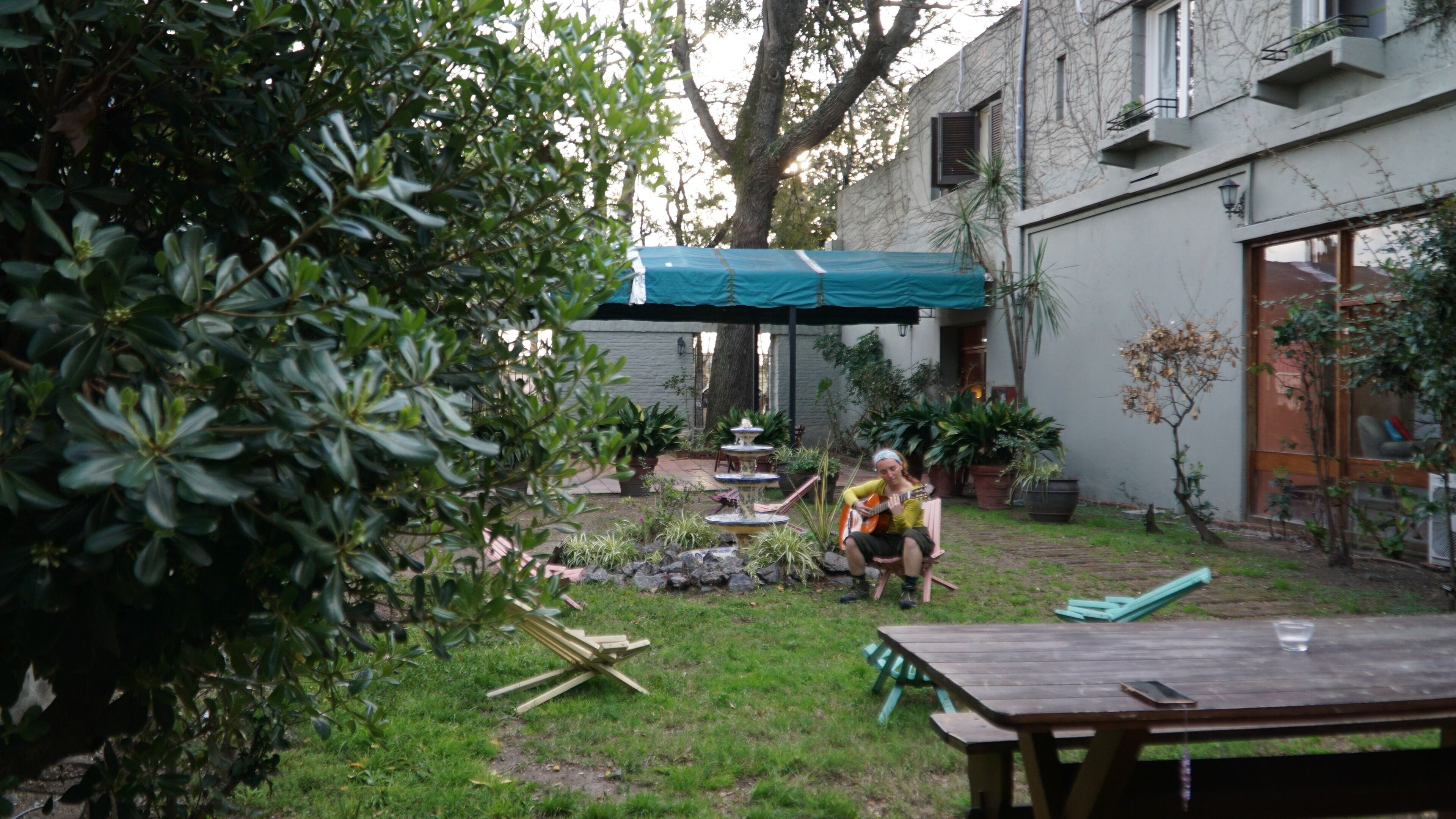 A patio area with a wooden table, a green umbrella, and a fountain.