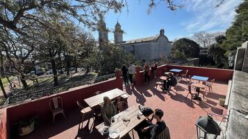 An outdoor patio with tables and chairs, surrounded by trees and a view of a historic building with towers.