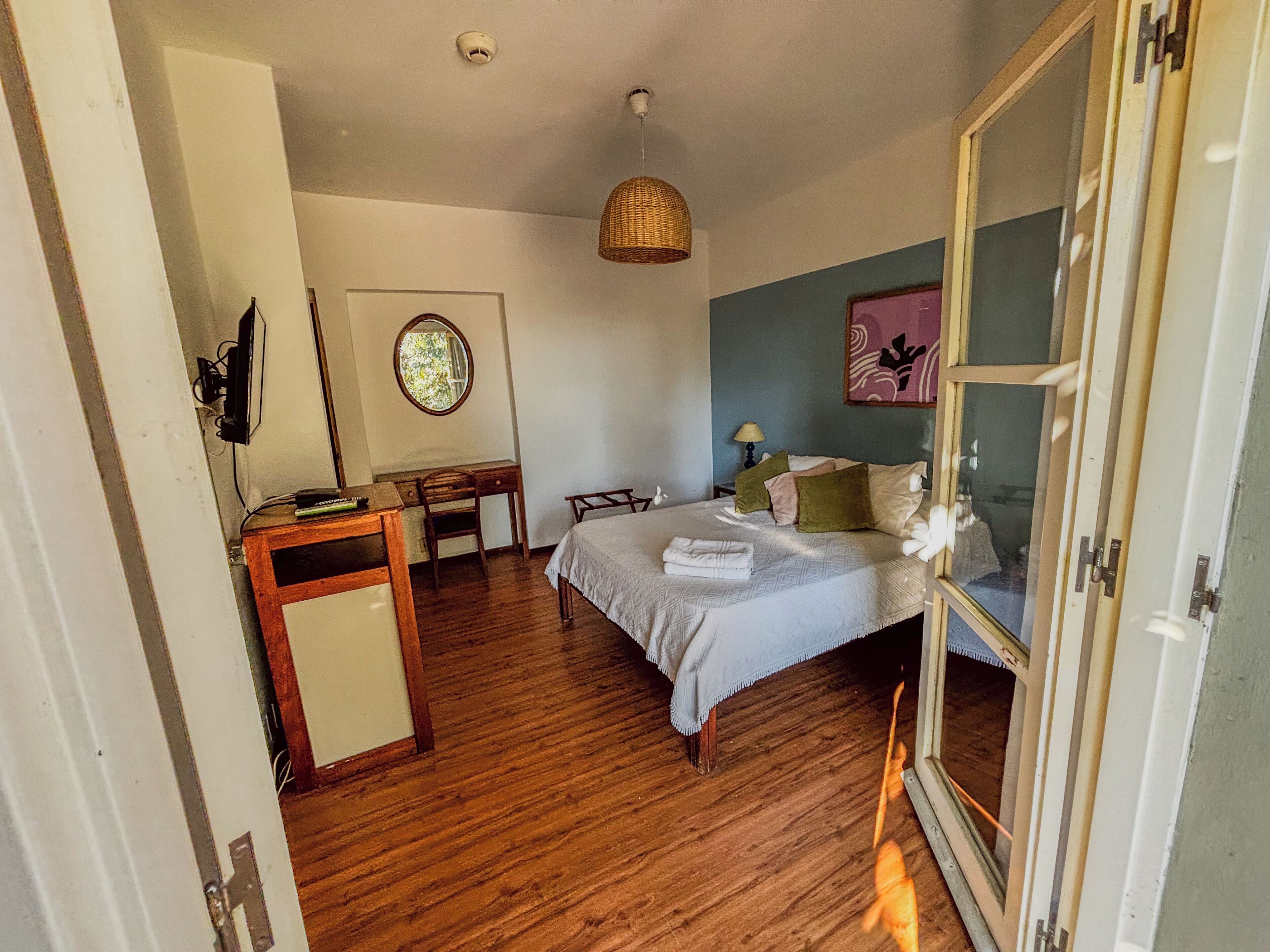 Un dormitorio con cama, mesita de noche, escritorio, silla y una lámpara colgante.