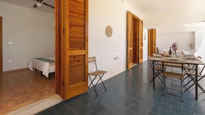 A spacious room with a dining table set for four, a ceiling fan, and a wooden door.