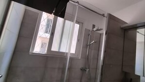 Un baño moderno con cabina de ducha de vidrio, una ventana que proporciona luz natural y un espejo grande.
