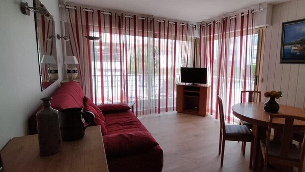 Una habitación acogedora con un sofá rojo, una mesa de comedor de madera con sillas, un televisor en un mueble y un cuadro en la pared.