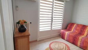 Una habitación con un sofá, una mesita de madera con un florero, un radiador y una ventana con persianas.