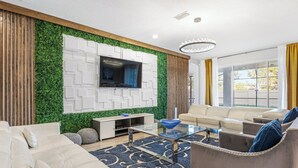 Een moderne woonkamer met een flatscreen televisie aan een witte muur, een beige bank, een bruine fauteuil en een glazen salontafel.