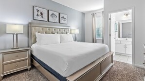 Een hotelkamer met een groot bed, twee nachtkastjes met lampen, een hoofdeinde met decoratieve details en uitzicht op de badkamer door een geopende deur.