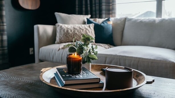 A cozy living room with a wooden coffee table, a lit candle, a book, and a mug. - The SpokeEasy DownTown Inn (Bentonville)