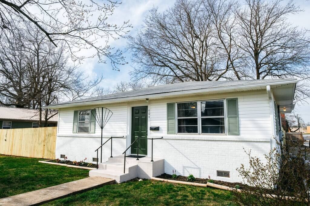 A single-story house with a front porch, a green door, and a small front yard.