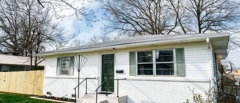 A single-story house with a front porch, a green door, and a small front yard.