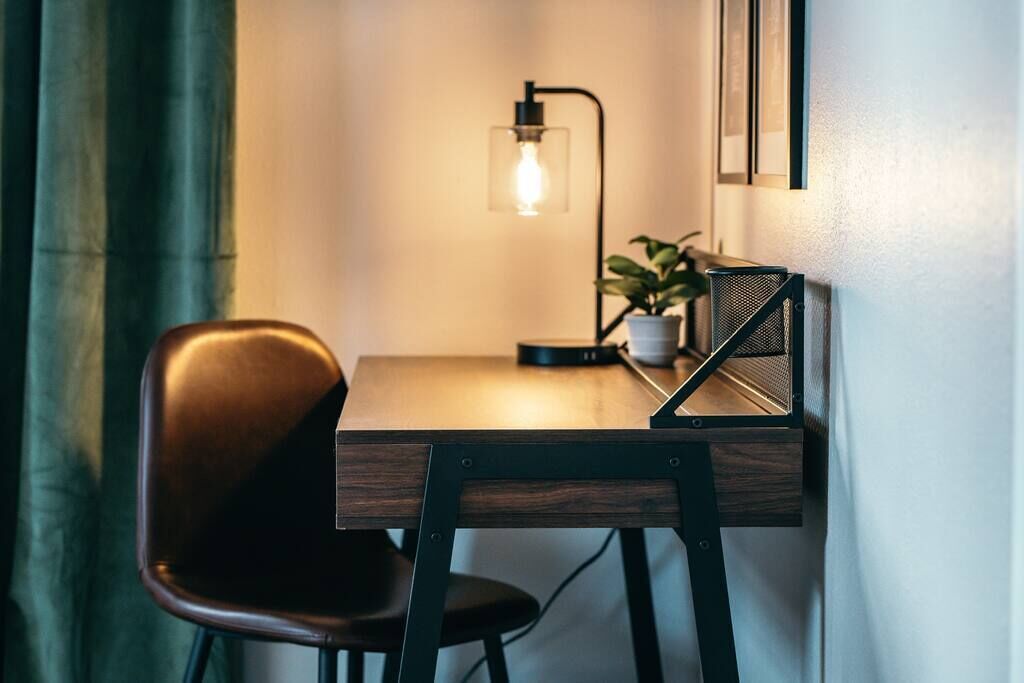 A small, dark wooden desk with a chair, a potted plant, and a wall-mounted lamp.