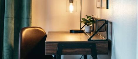 A small, dark wooden desk with a chair, a potted plant, and a wall-mounted lamp.
