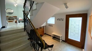 Un escalier avec une rampe noire et une main courante en bois, menant à un palier où se trouvent un banc blanc et une petite table.