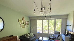 Un espace repas comprenant une table, des chaises, un lustre et une vue dégagée sur l’extérieur grâce à de grandes fenêtres.