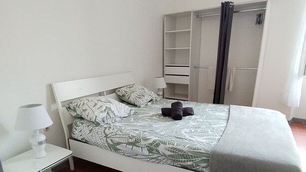 Una camera da letto ordinata con un letto, un comodino con una lampada, un armadio e un pavimento piastrellato.