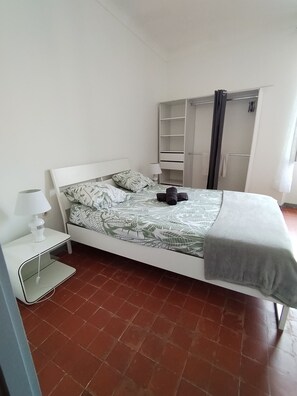 Une chambre bien rangée, avec un lit, une table de chevet dotée d’une lampe, une armoire et un sol carrelé.