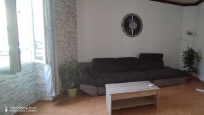 Un soggiorno con parete in pietra, un divano scuro, un tavolino in legno, una sveglia a parete e un termosifone.