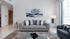 Ein modernes Wohnzimmer mit einem grauen Sofa, dekorativen Kissen, einem schwarzen Teppich und einem großen abstrakten Gemälde an der Wand.