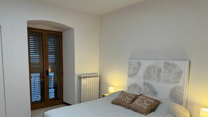 Ein Schlafzimmer mit Bett, Nachttisch, Lampe, Heizkörper und einer Tür mit Jalousien.