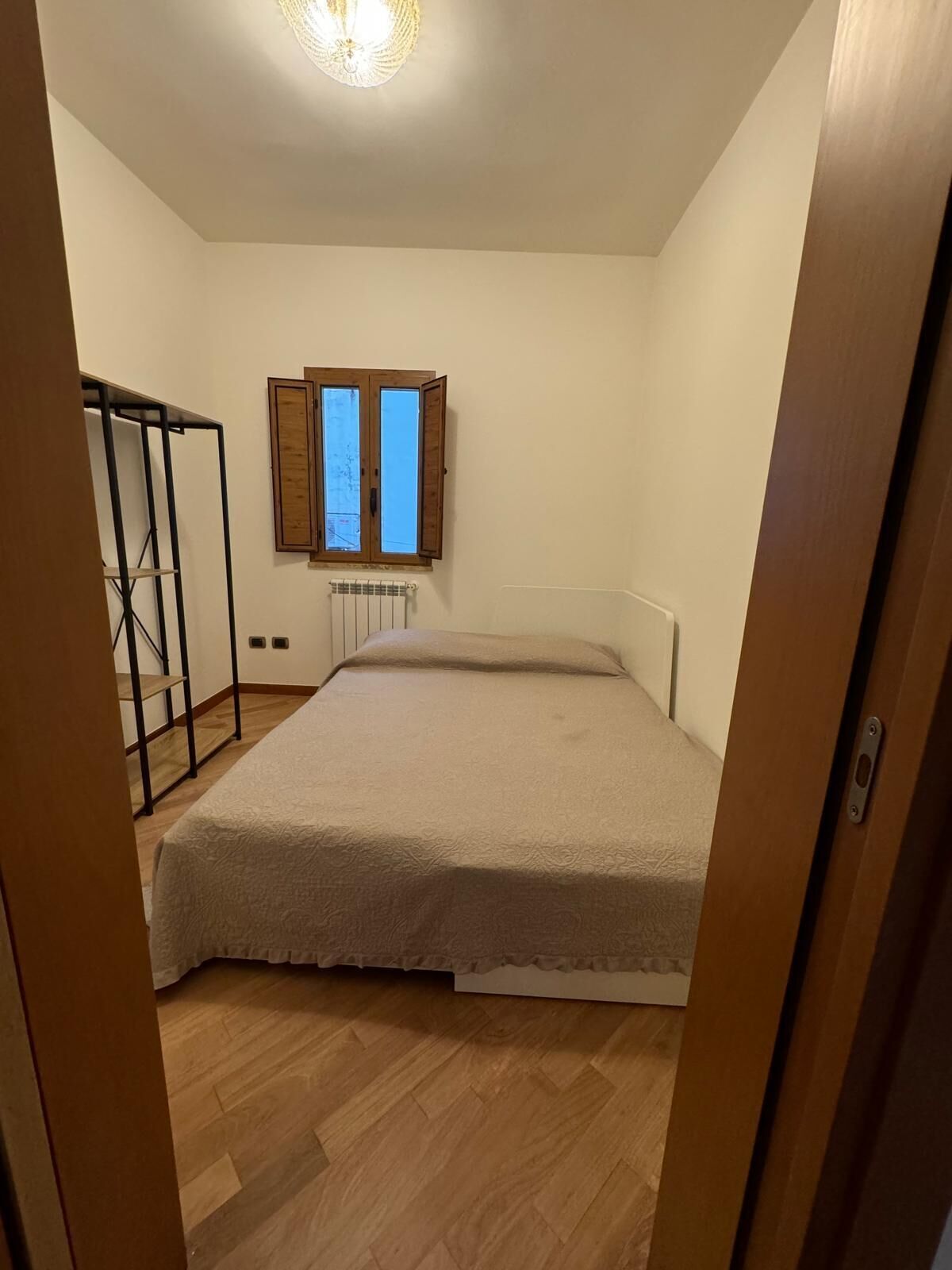 A bedroom with a bed, a radiator, a window, and a wooden floor.