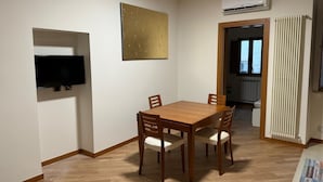Ein Essbereich mit Holztisch und -stühlen, einem an der Wand befestigten Fernseher und einer Klimaanlage.
