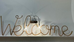 Eine Wandtafel mit der Aufschrift "Welcome“, in der Mitte eine Leuchte.