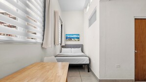 A bedroom with a bed, a wooden table, a window with blinds, a painting on the wall, and a door. - New! Penthouse Studio C in heart of Condado (San Juan)