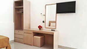 A room with a wooden wardrobe, a vanity with a mirror, a small stool, and a bed. - Graha Wisata (Kotabumi)